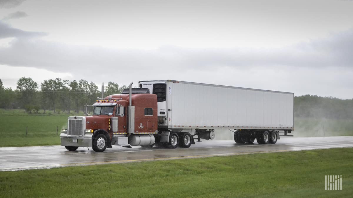 Tractor-trailer heading down wet highway.