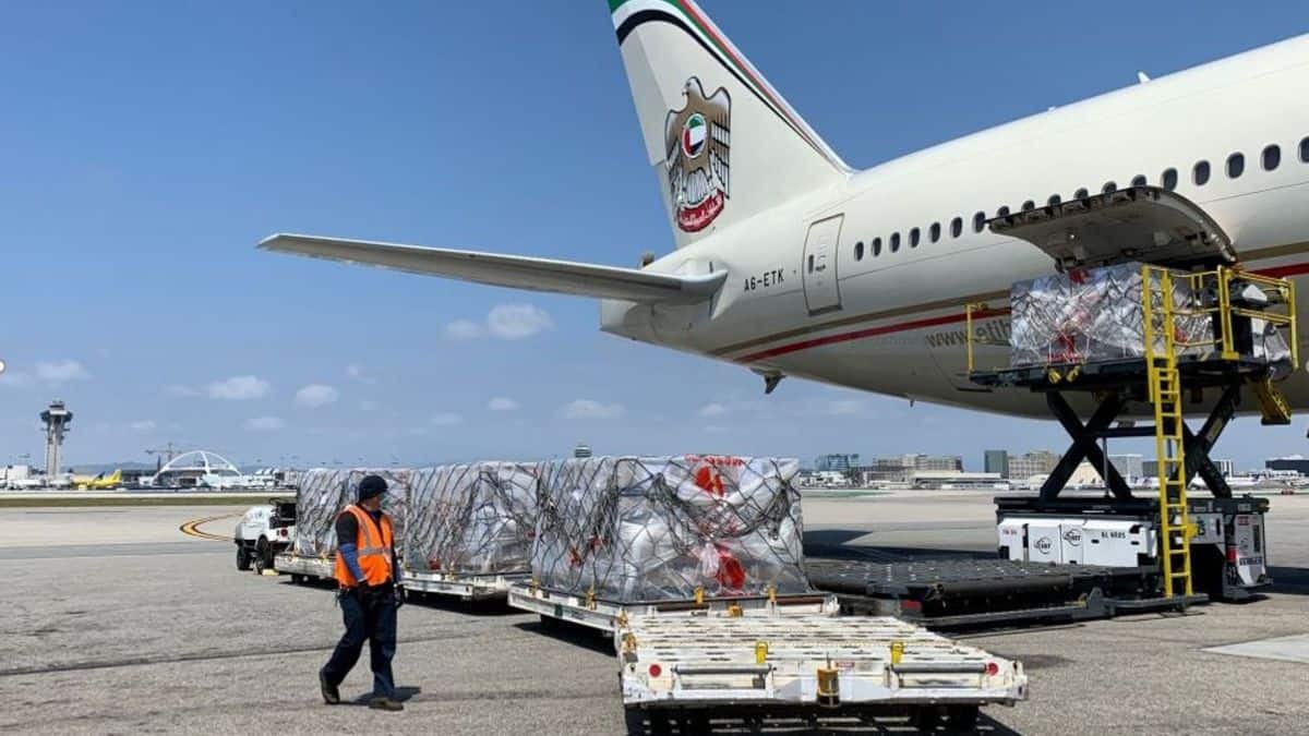 Cargo on pallets on airport tarmac waiting to be loaded in back door of large plane on sunny day.