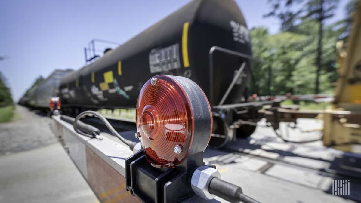 A photograph of a tank car by a rail crossing.