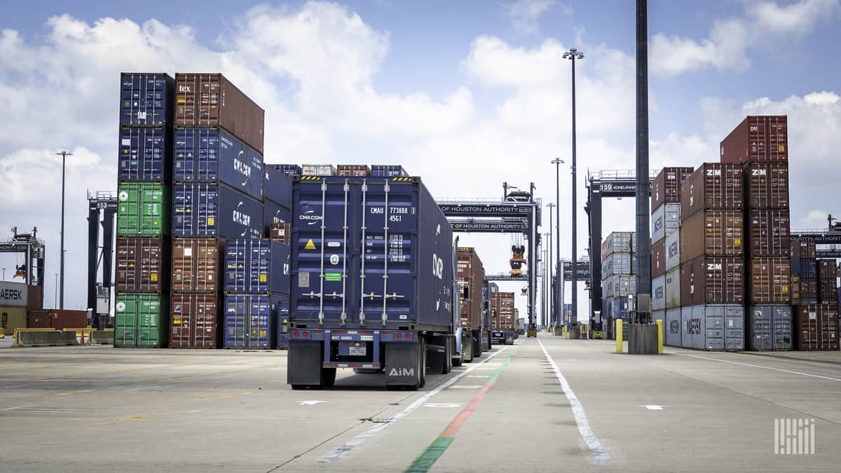 Trucks lined up between stacks of intermodal containers.