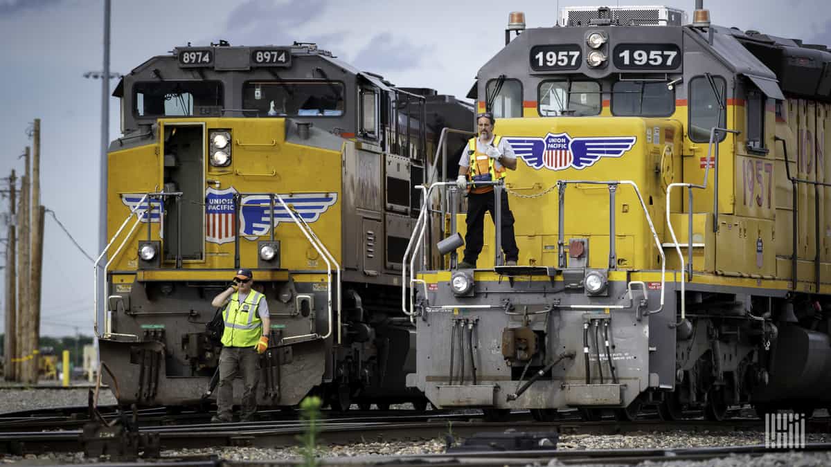 A photograph of two locomotive engines. Two men are standing in front of the locomotives.