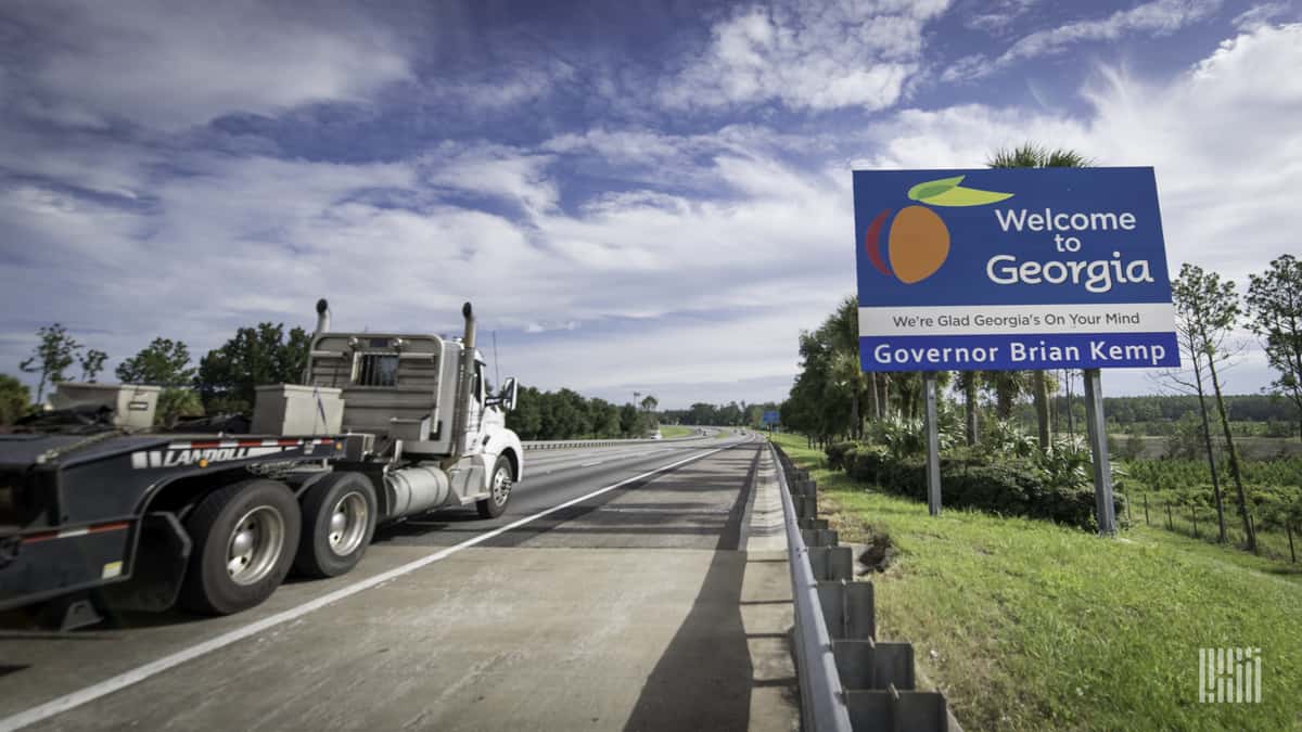 A flatbed commercial truck passes a sign that reads "Welcome to Gerogia"