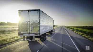 Tractor-trailer heading down desert highway with bright sunshine across the sky.