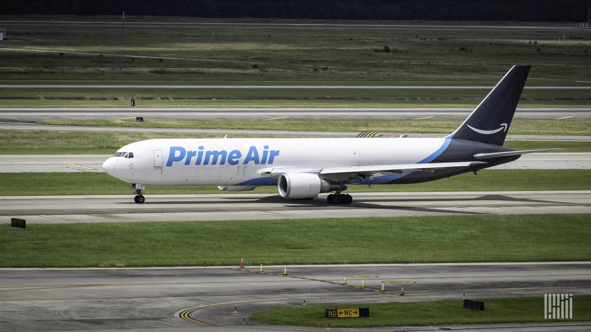 A white Amazon Air plane with light-blue lettering on runway.