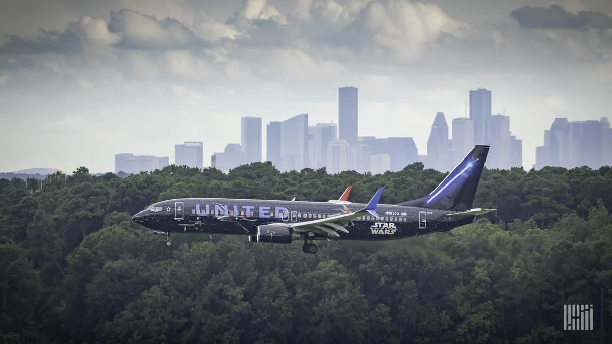 A dark blue United Airlines jet comes in for landing, side view right above the tree tops. United posted a $1.6 billion loss Tuesday.