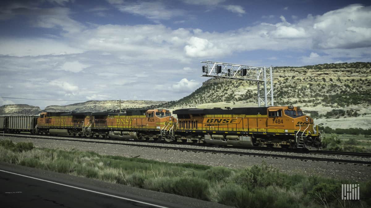 A BNSF train travels by a desert mountain range.