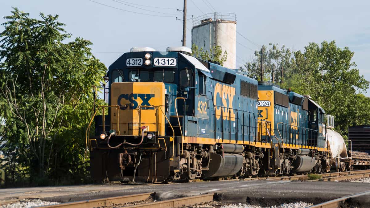 A photograph of a CSX train. There is a line of trees behind the train and alongside the train track.