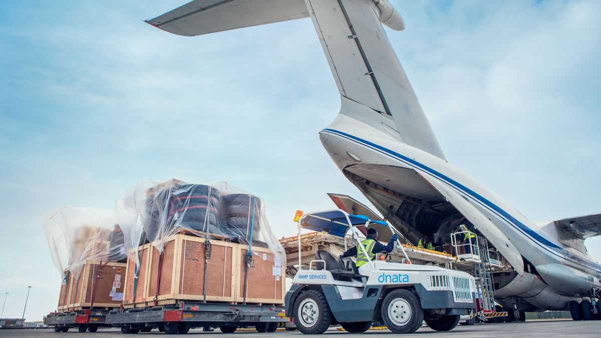 A white cargo tug moves a shipment after unloading from the rear ramp of a massive cargo plane. dnata is an airport services operator and faces congestion problems at Sydney Airport.