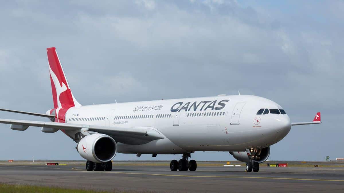 A large white Qantas jet with red tail on tarmac. Qantas is dealing with a COVID outbreak at one of its facilities.