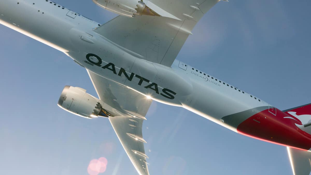 A big Qantas jet takes off in bright skies right over photographer, with logo clearly seen on bottom of fuselage. Qantas' international business is suffering.