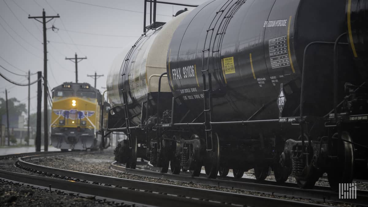 A photograph of a Union Pacific train behind a train of tank cars. They are at a rail yard.