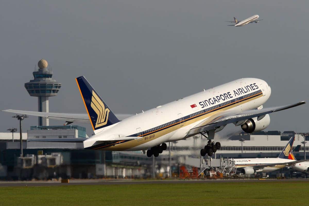 White Singapaore Airlines jetliner with blue tail lifts off from runway with airport control tower in background. Singapore Airlines is helping the World Food Program.
