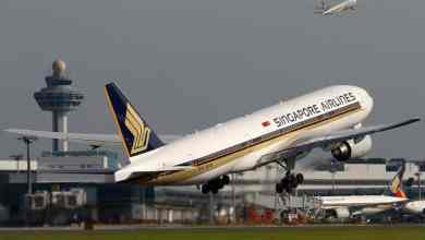 White Singapaore Airlines jetliner with blue tail lifts off from runway with airport control tower in background. Singapore Airlines is helping the World Food Program.