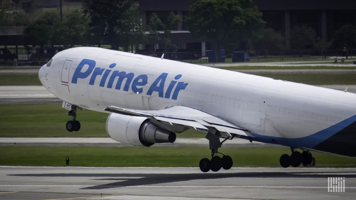 A white Amazon cargo jet with front wheel lifting off on takeoff.