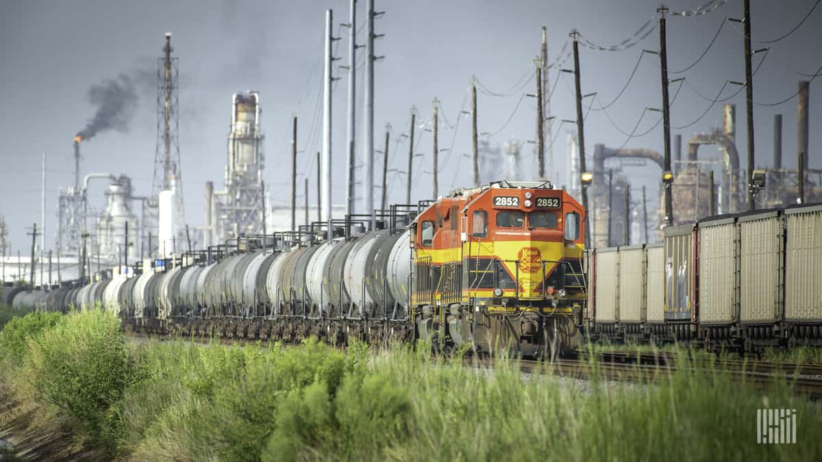 A photograph of a Kansas City Southern train traveling by an industrial yard.