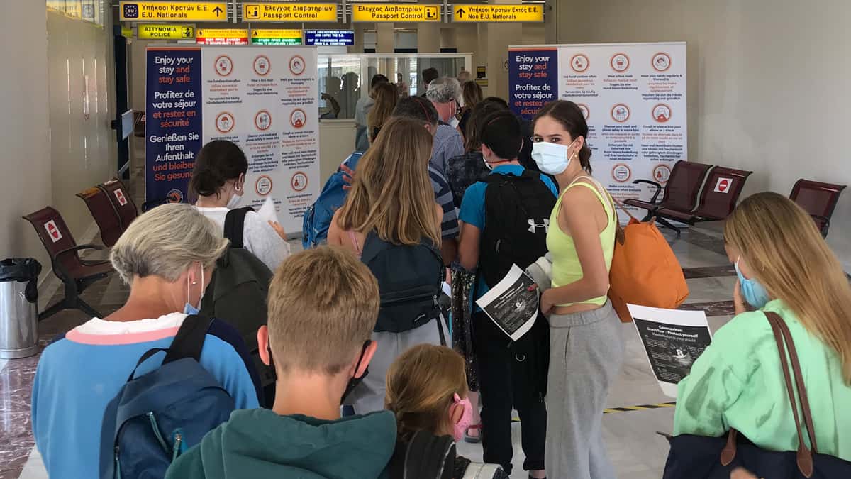 Travelers wearing masks, waiting to go through checkpoint at airport in Greece.