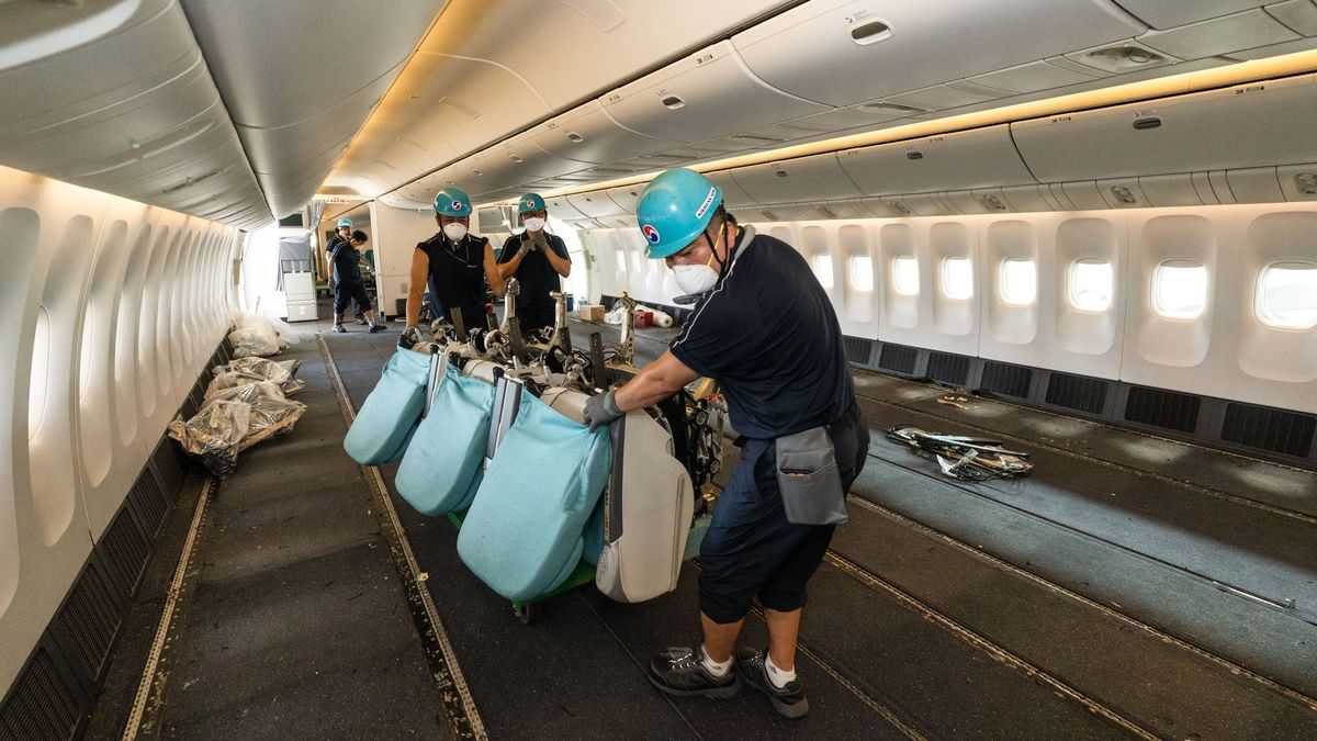 Korean Air technicians inside a jet cabin lift out the last seats to make room for floor-loading cargo.