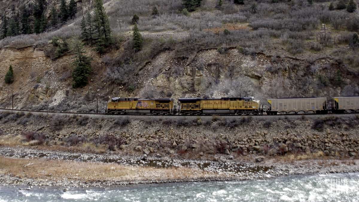 A photograph of a Union Pacific train traveling by a rocky mountainside.