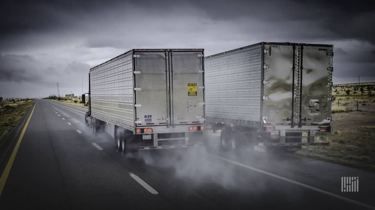 Two tractor-trailers heading down a wet highway, side-by-side.