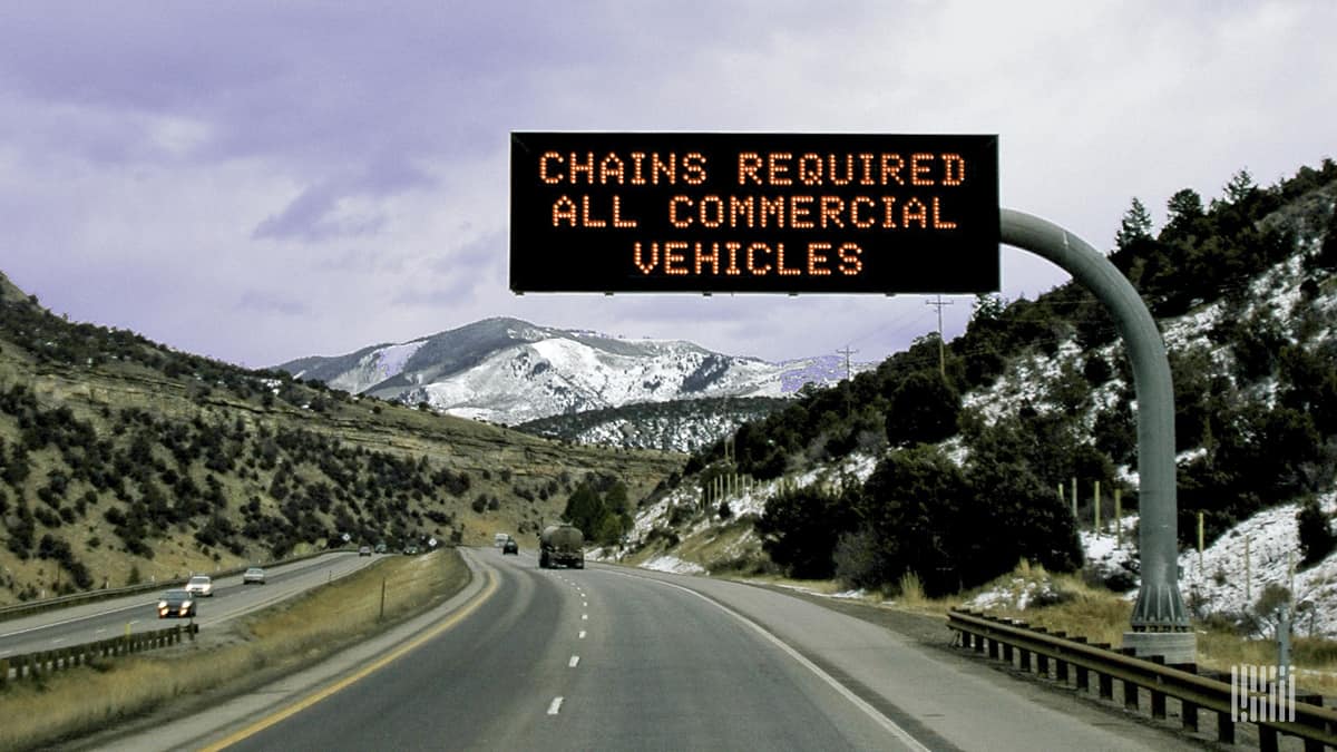 "Chains required" road sign along a snowy mountain road.