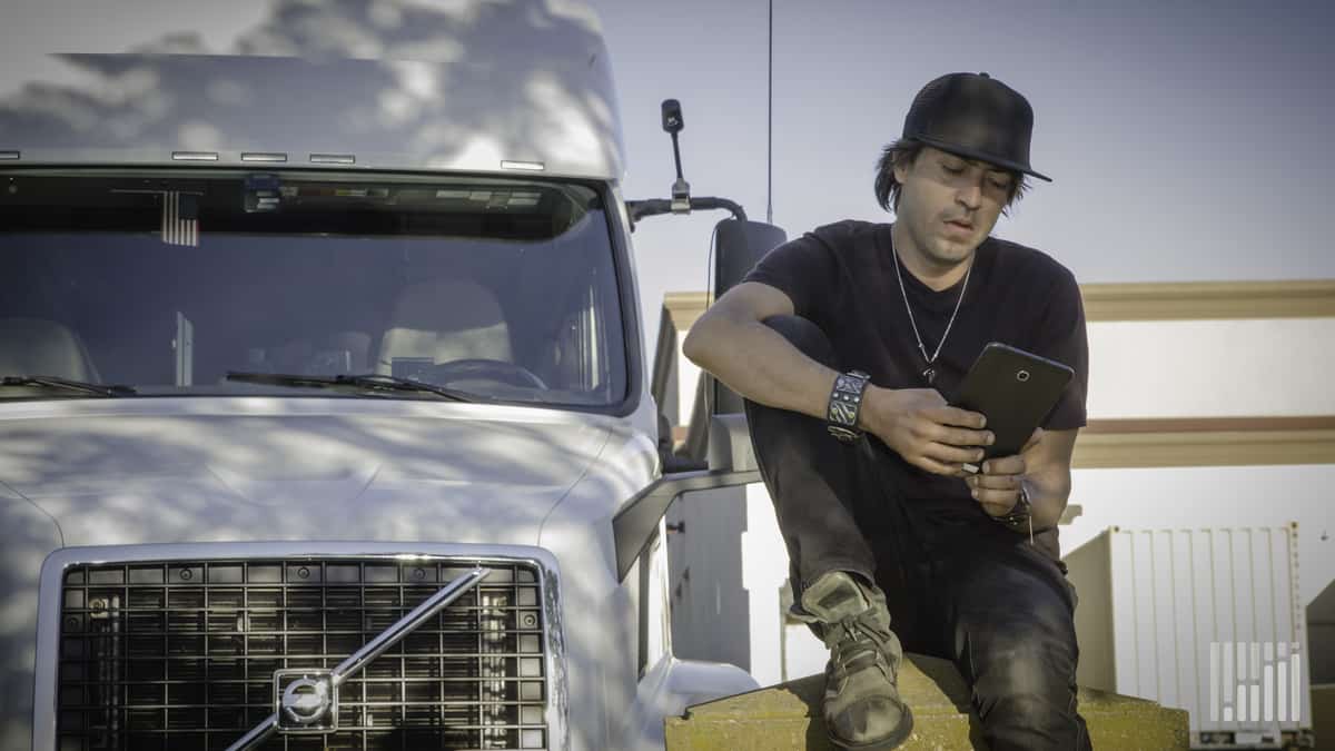 Driver leaning on his truck while using his tablet.