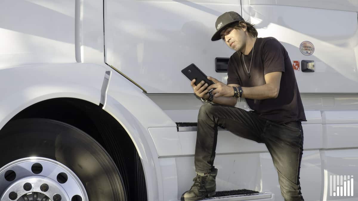 Driver leaning on his truck while using his tablet.