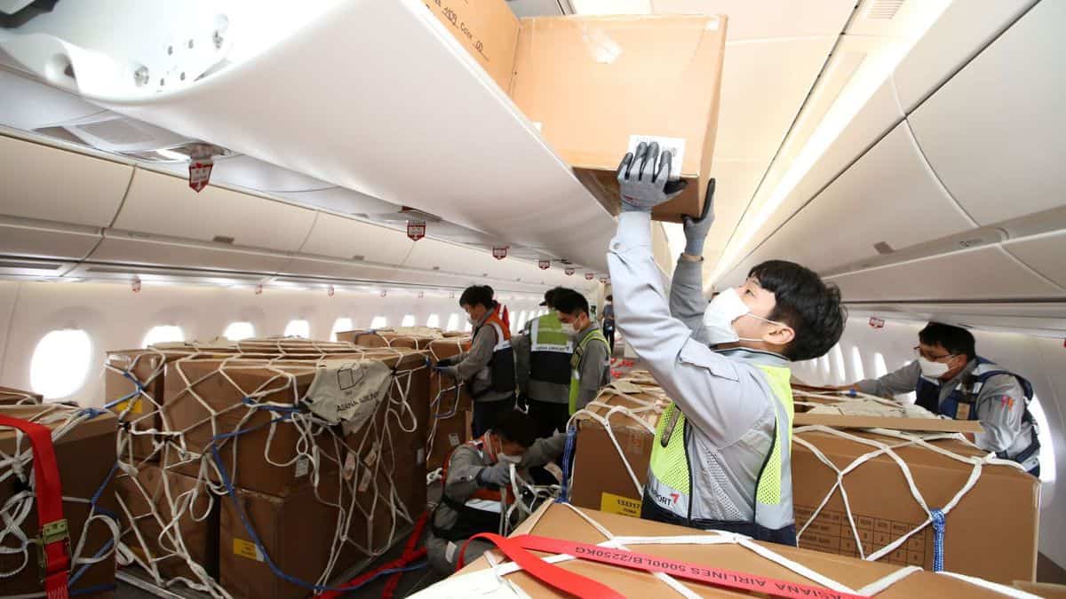 Boxes being loaded in overhead bins and on floor of passenger plane with no seats.