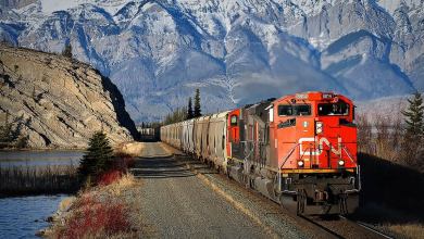 A photograph of a CN train traveling away from a high mountain range.
