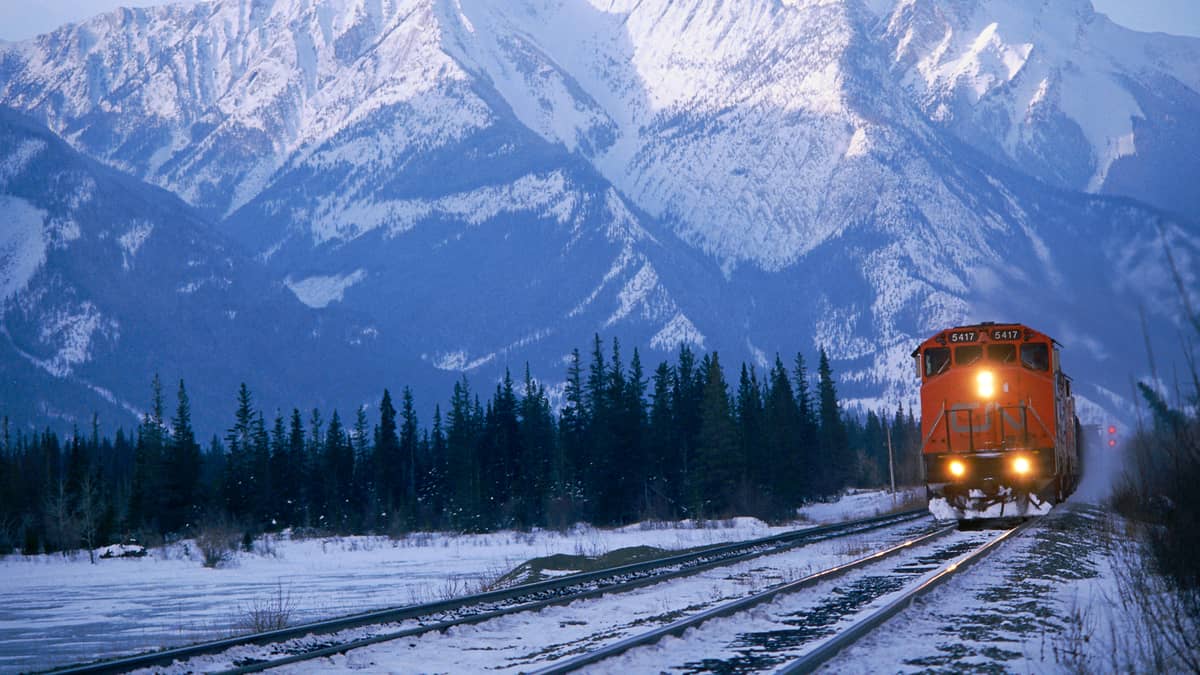 A photograph of a CN train heading away from a snow-capped mountain.