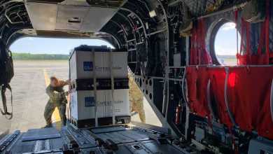 National Guard troops unload a large pallet out the back of a helicopter.