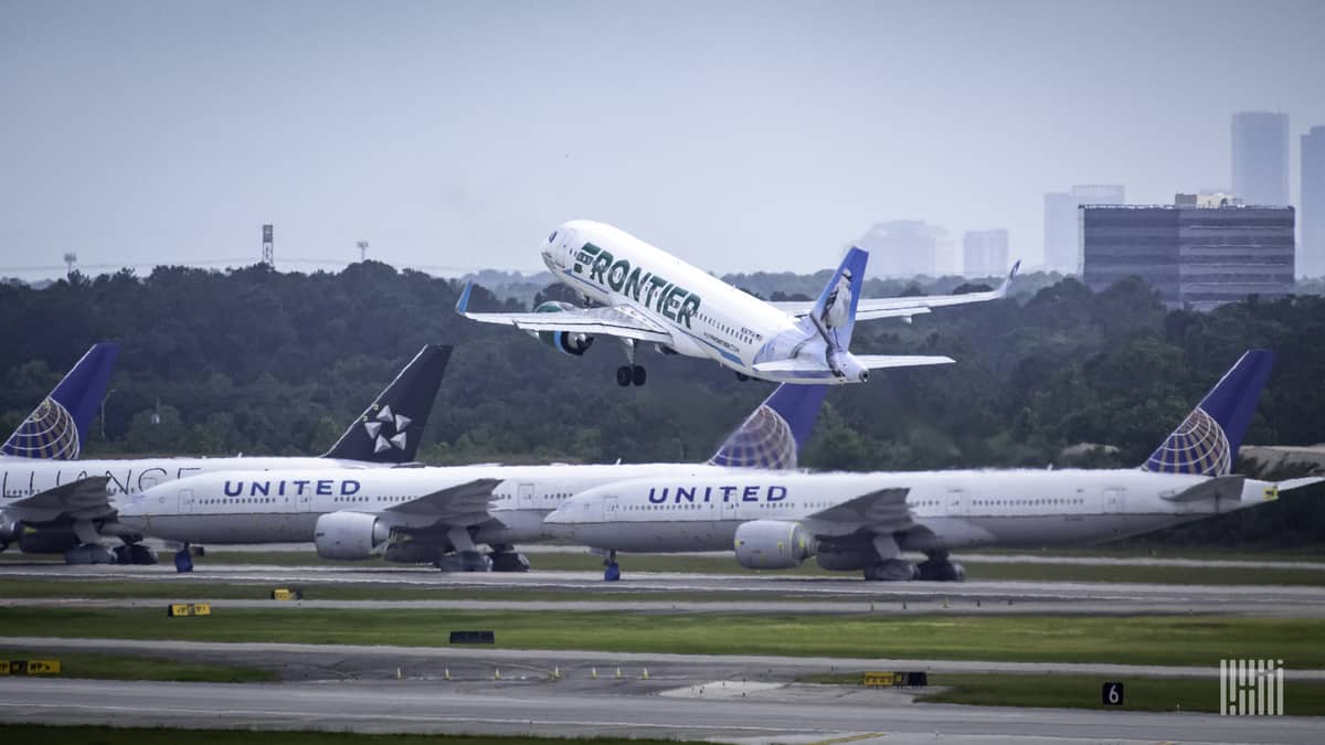 A white jet takes off with other planes sitting in the foreground and buildings from downtown Houston in the background.