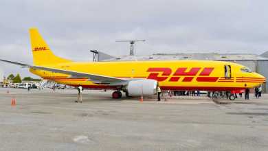 Mustard-yellow DHL freighter jet sitting at airport.
