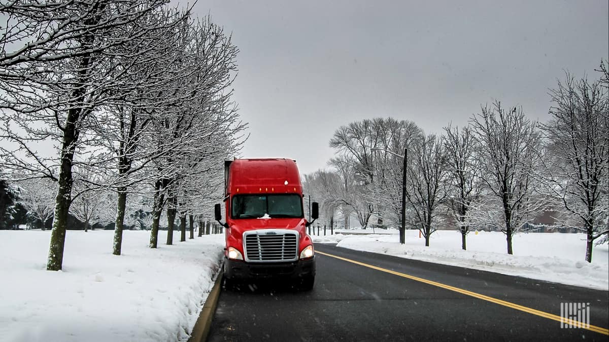 Tractor-trailer pulled over on slick road, with snow-covered grass.