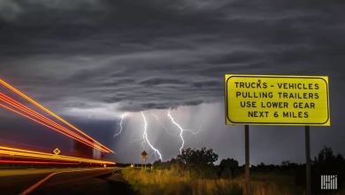 Tractor-trailers heading down a highway, with lightning across a dark sky.