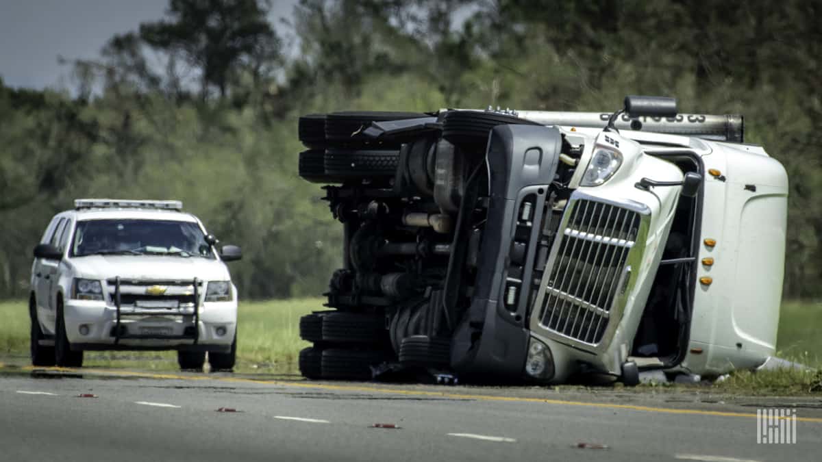 Flipped tractor-trailer on the side of a road.