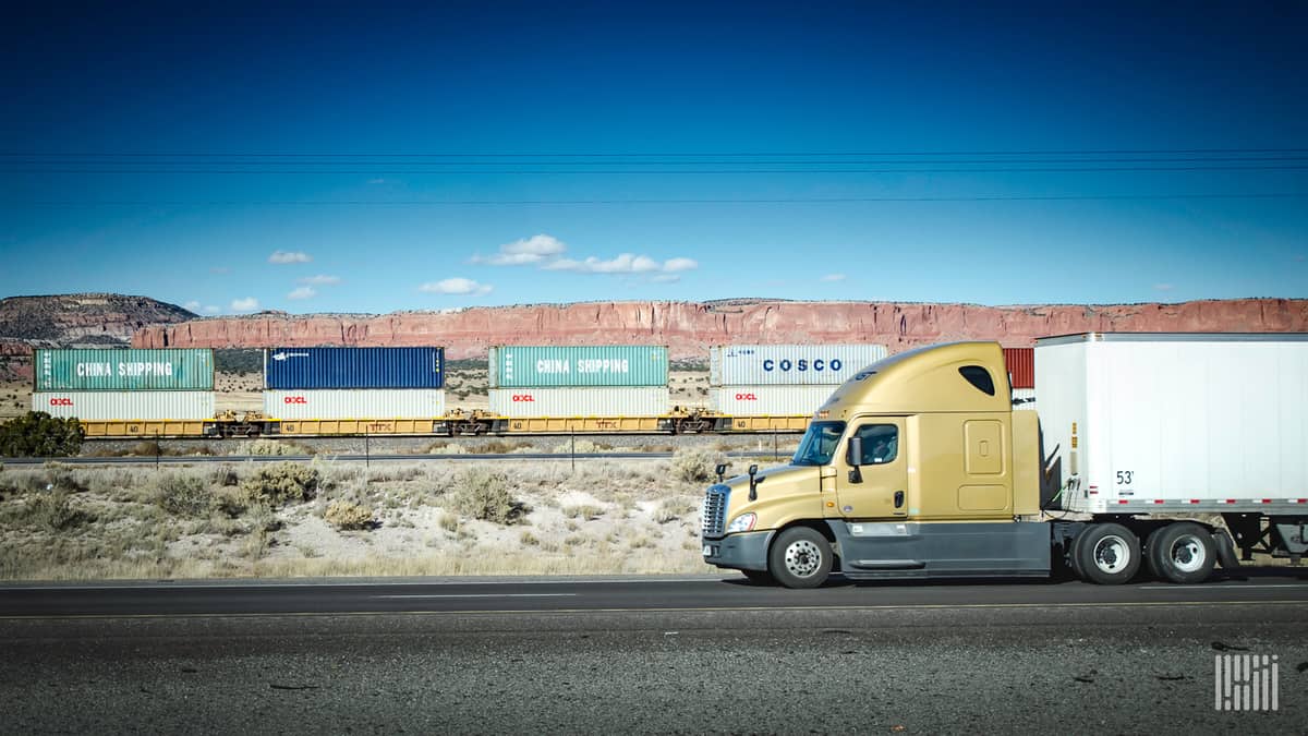 A photograph of a truck driving alongside a freight train.