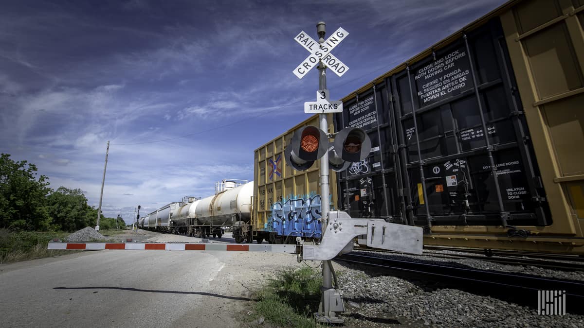 A photograph of a train passing by a rail crossing.