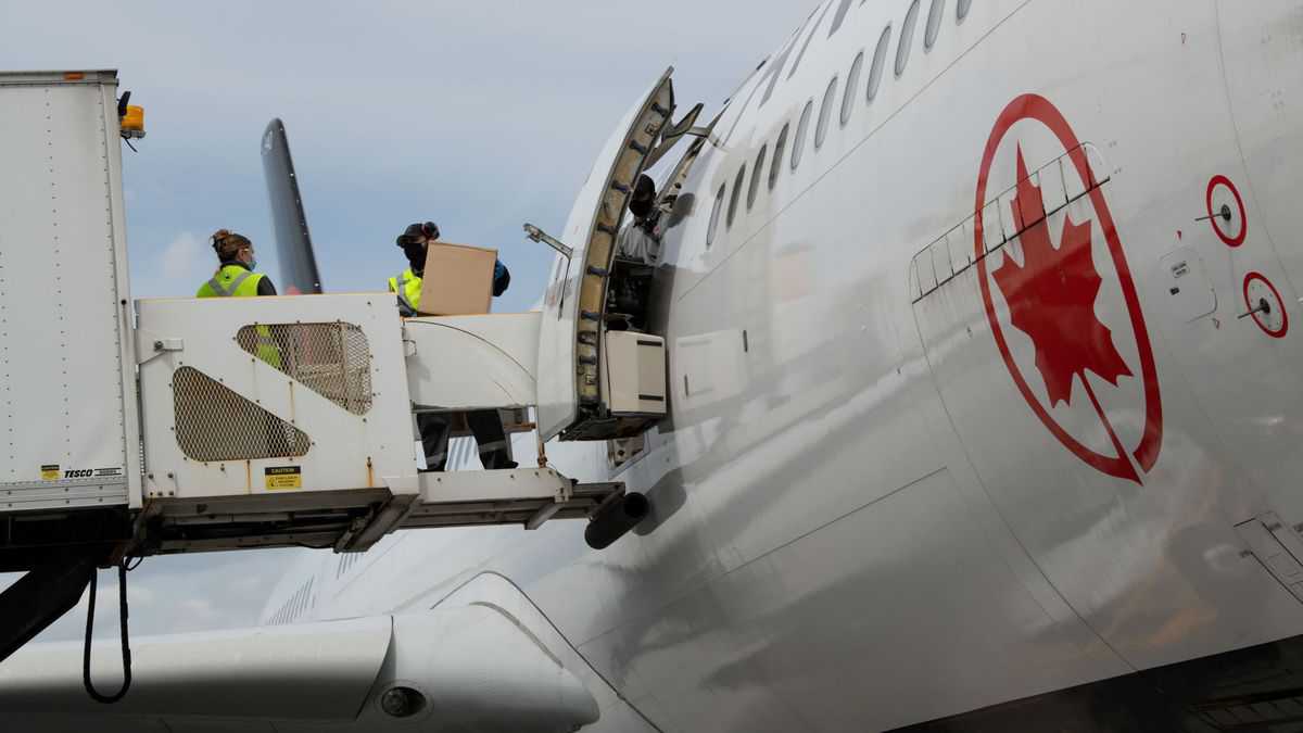 Cargo being loaded from hydraulic lift through side door of white Air Canada jet.