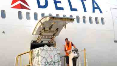 A pallet of cargo on a hydraulic lift gets moved into the side door of a white Delta Air Lines airplane.