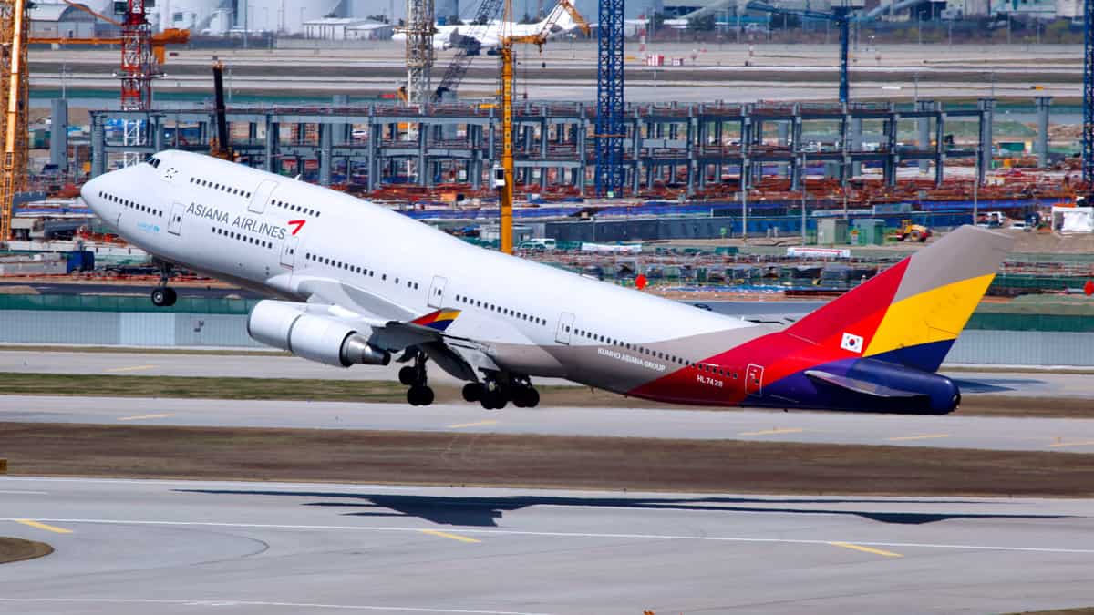 An Asiana jumbo jet with white fuselage and multicolored tail lifts off from runway.