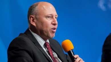 White man with receding hair speaking into handheld microphone at conference.