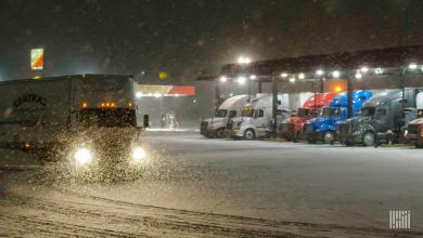 Tractor-trailers at a truck stop on a snowy night.