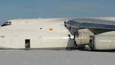 A big white freighter aircraft lies in snow at end of runway with damaged engine after emergency landing.