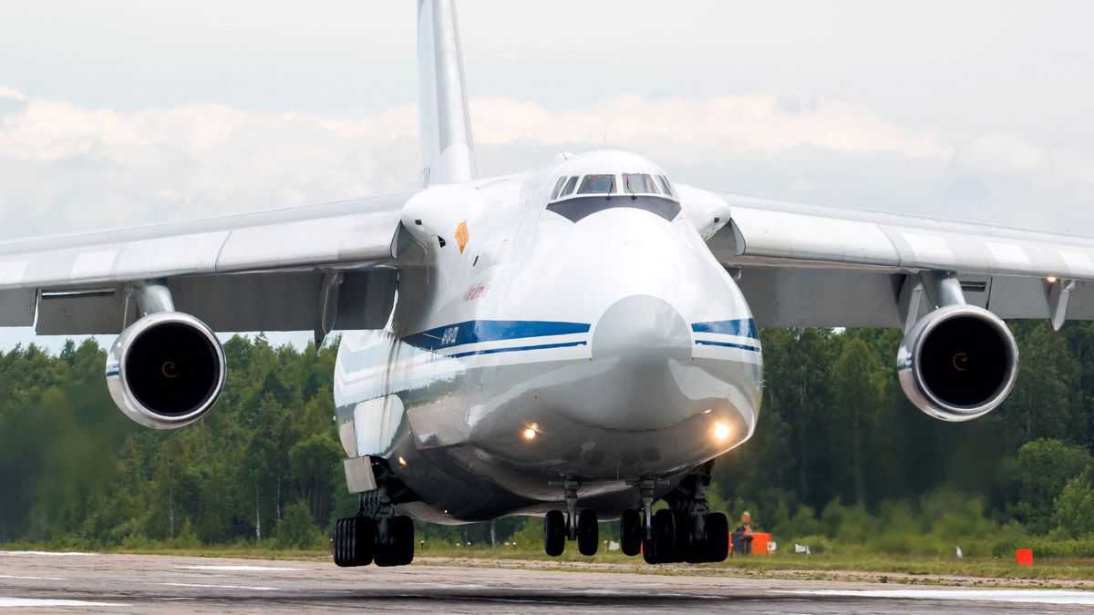 A massive white cargo jet inches from touching down on runway.