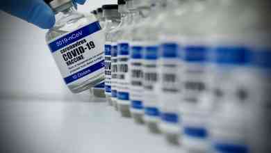 A gloved-hand reaches for vial of a COVID-19 vaccine dose. The distribution of COVID-19 vaccines could begin in mid-December