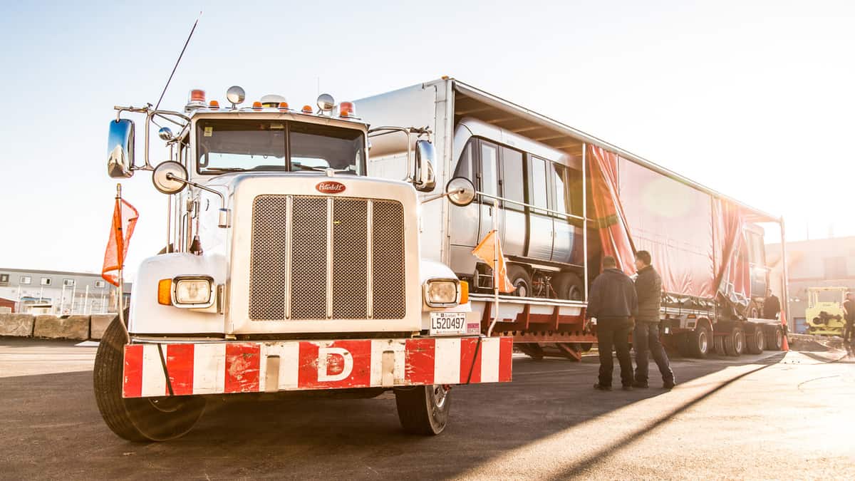 A semi-truck of Watson Transport with a trailer containing a rail car. QSL became full owner of Watson.