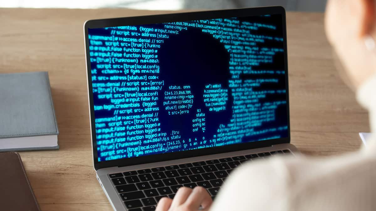 A laptop showing computer code and the outline of a skull to illustrate a ransomware attack.