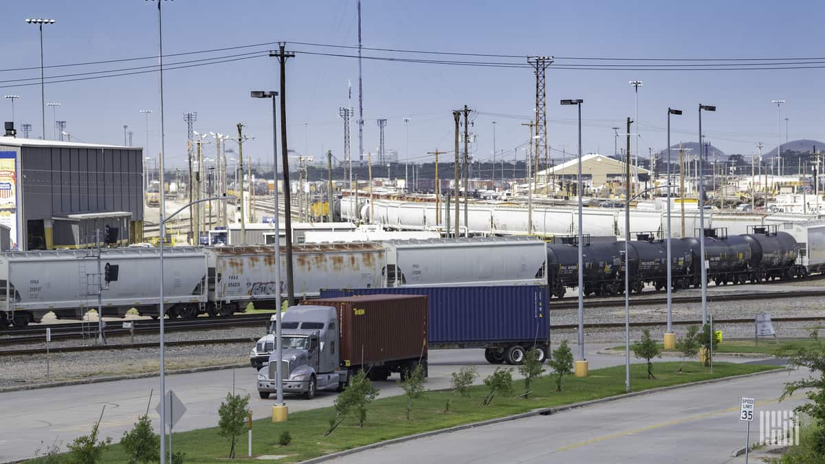 A photograph of a truck passing by a rail yard.