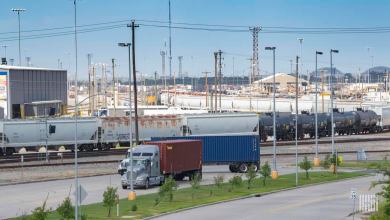 A photograph of a truck passing by a rail yard.