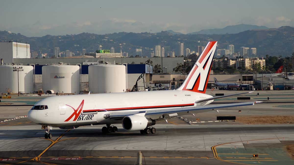 A white ABX Air jet moves down runway with giant fuel tanks in the background.